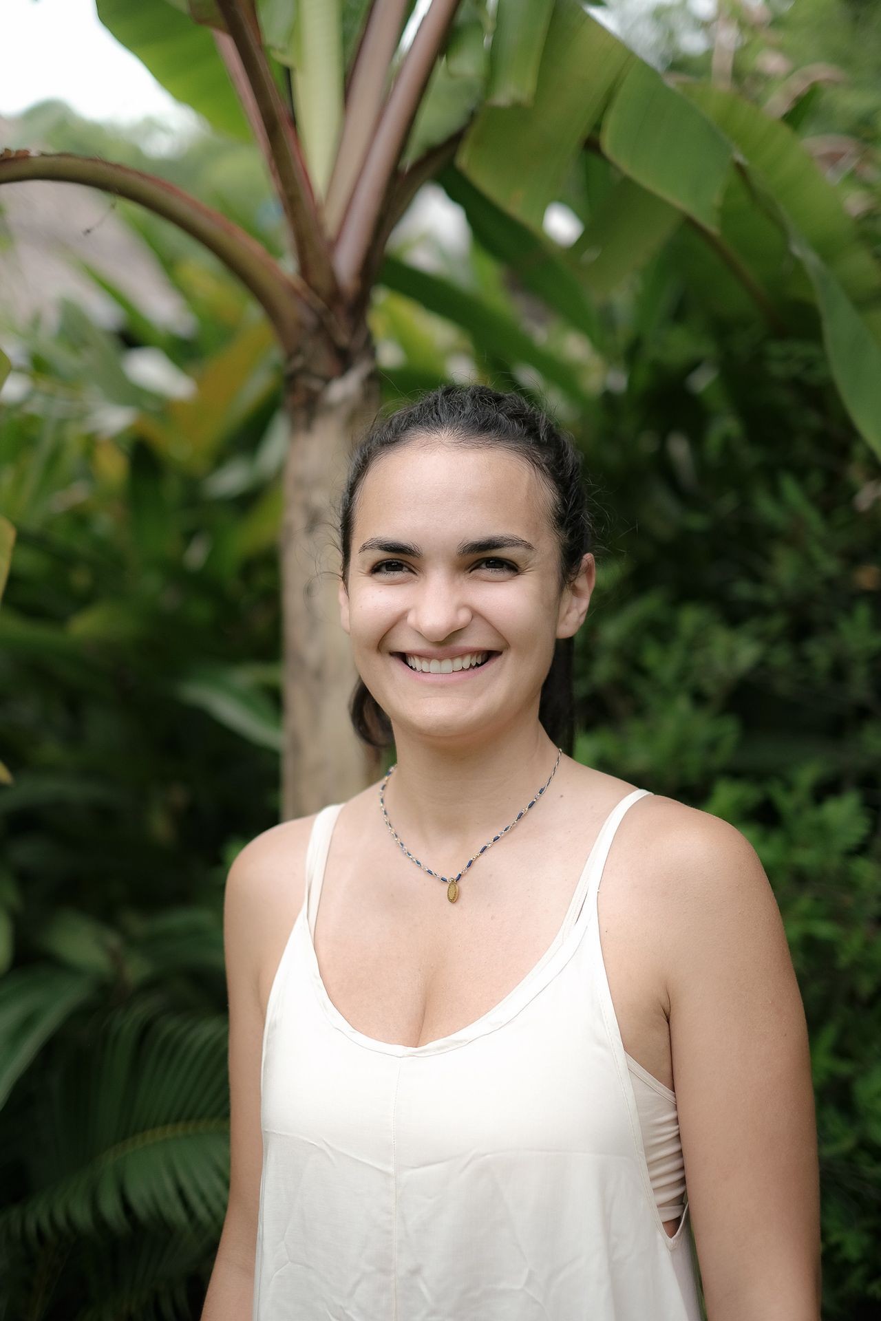 Smiling person standing outdoors with green leaves in the background.
